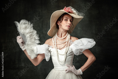 Creative portrait of young beautiful girl elegant dress of medieval fashion style with veer isolated on dark background. Comparison of eras concept, flemish style.