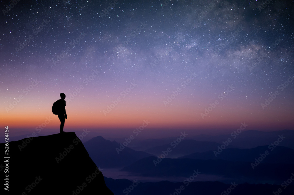 Silhouette of young traveler with backpack standing and watched the star, milky way and night sky alone on top of the mountain. He enjoyed traveling and was successful when he reached the summit.