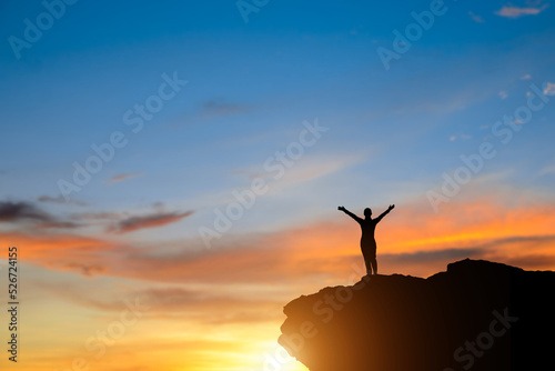 Silhouette of young woman traveler with backpack standing alone on top of the mountain and watched beautiful view sunset. She enjoyed traveling and was successful when he reached the summit.