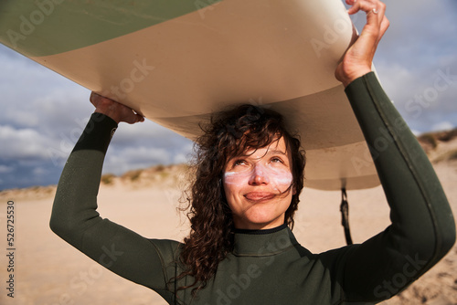 Photography Cute woman with sunscreen at her chicks carrying surfboard on head and enjoying