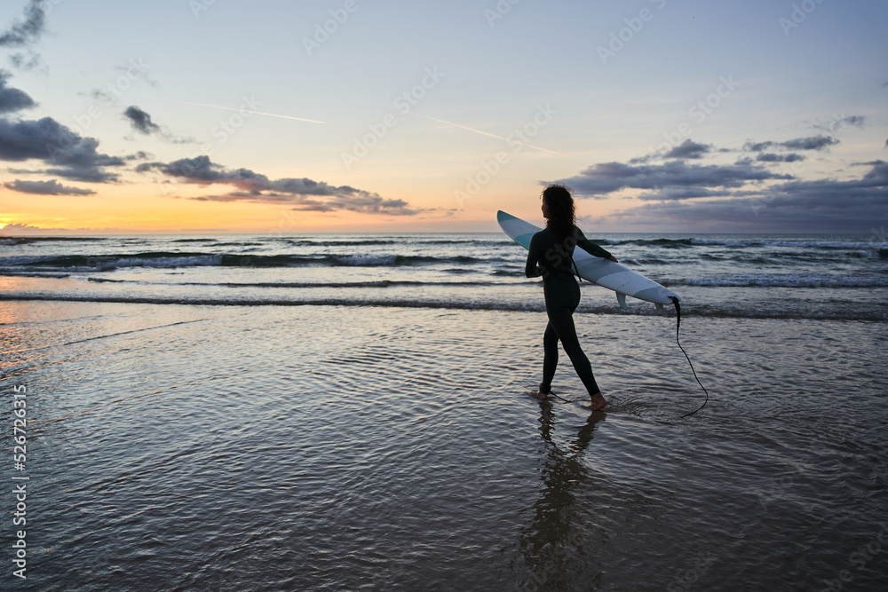Silhouette view of the young woman with surfboard going for surfing in the sea Silhouette view of the young woman with surfboard going for surfing in the sea