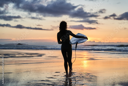 Surfer woman silhouette holding surfboard on summer beach during the sunset