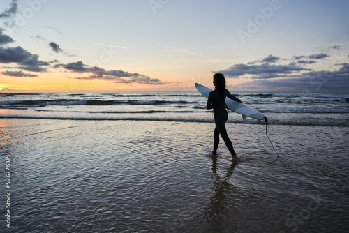 Silhouette view of the young woman with surfboard going for surfing in the sea