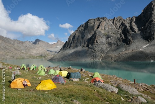 Colorful tents on bank of Lake Ala-Köl (Ala-kol, Ala-kul) in Tien Shan mountains in west of Kyrgyzstan, Asia. Cyan color of lake under steep mountaines. Touristic destination for trekking.