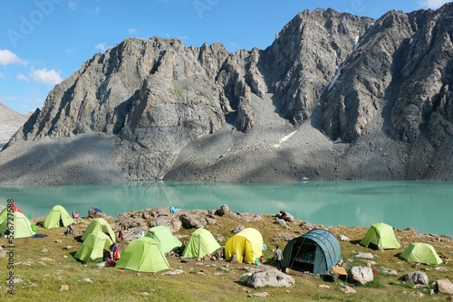 Colorful tents on bank of Lake Ala-Köl (Ala-kol, Ala-kul) in Tien Shan mountains in west of Kyrgyzstan, Asia. Cyan color of lake under steep mountaines. Touristic destination for trekking.