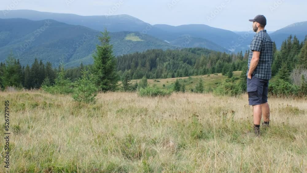 middle-aged beared hiker man in plaid shirt is on the mountain glade and have a pleasure of view of the mountains middle-aged beared hiker man in plaid shirt is on the mountain glade and have a pleasure of view of the mountains