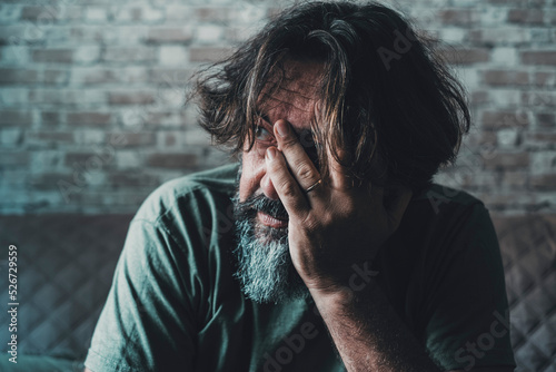 Desperate and stressed man touching his face with hand and looking outside at home. Problems and worried people indoor. End of relationship and love for husband sitting on toe sofa. Economy failure