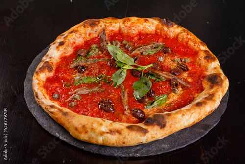 Pizza napoletana gourmet con sugo di pomodoro, basilico fresco, acciughe, olive nere e origano servita in una pizzeria napoletana