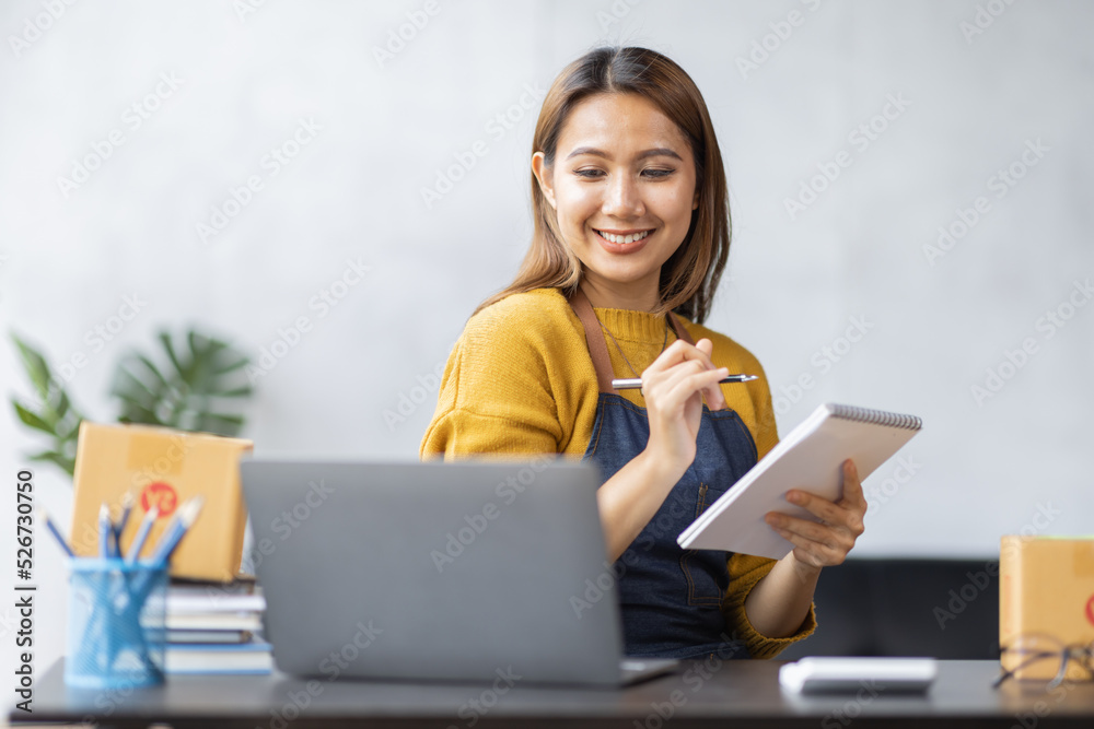 Fototapeta premium Asian woman look like india girl working SME business at workplace at home. use laptop checking customer order online shipping boxes, freelance SME entrepreneur online business idea.