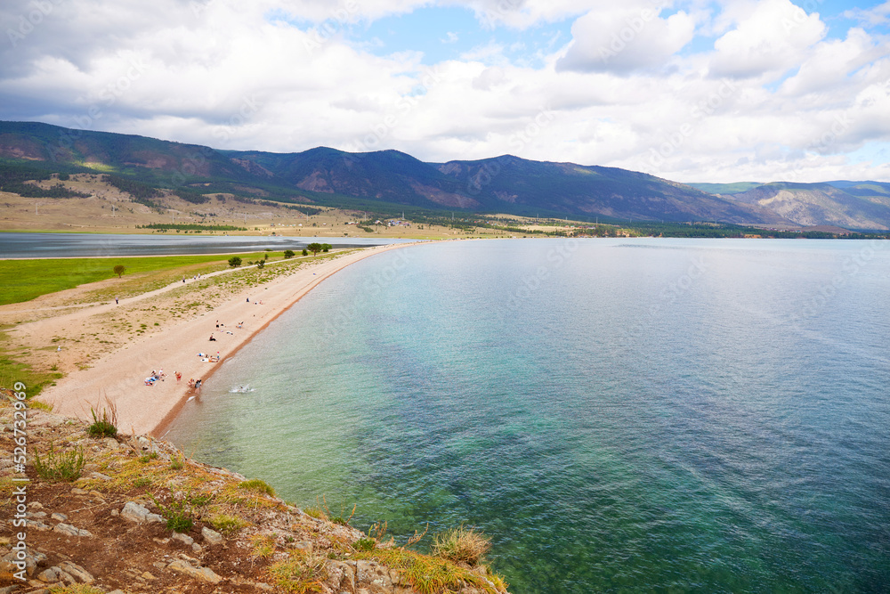 Lake Baikal in summer. View from Cape Uyuga to the beach and the bay near the village of Kurma. Tourists sunbathe and relax on the beach. Beautiful turquoise color of the water. 