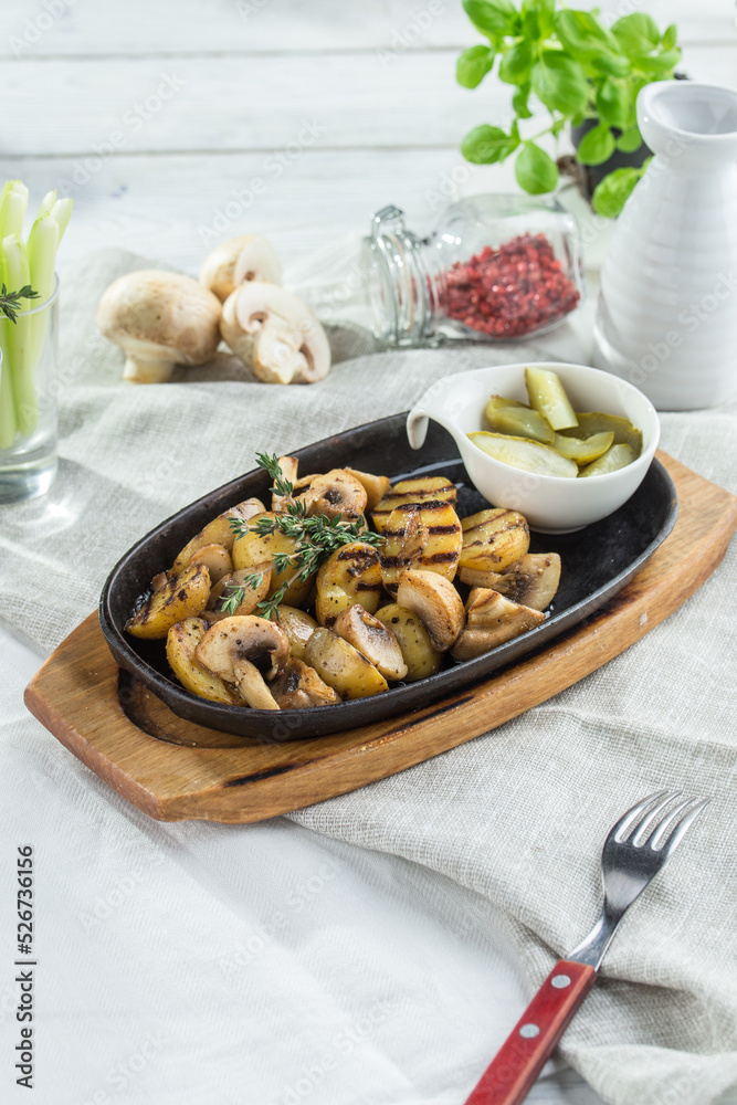 Fried potatoes with mushrooms and pickles on white table background
