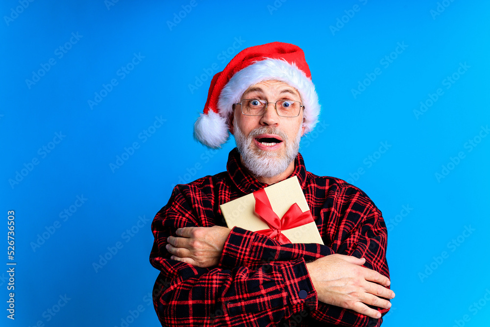 an elderly and well-groomed man in a plaid shirt and santa hat in blue studio background an elderly and well-groomed man in a plaid shirt and santa hat in blue studio background