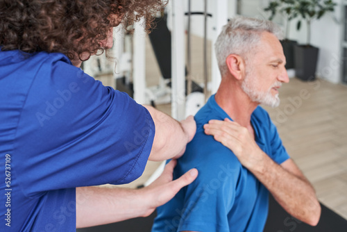 Therapist stretching arm and back of elderly man during the physical therapy at the hospital