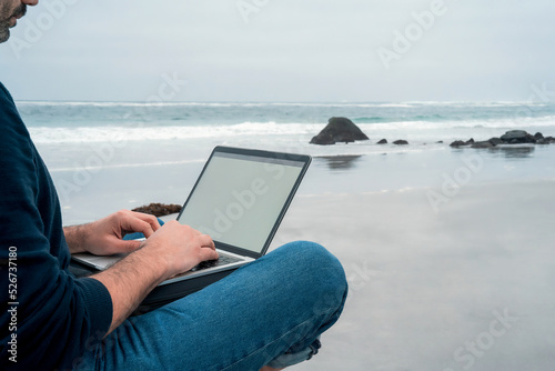 unknown man sitting relaxed on the beach with a laptop working, hands view