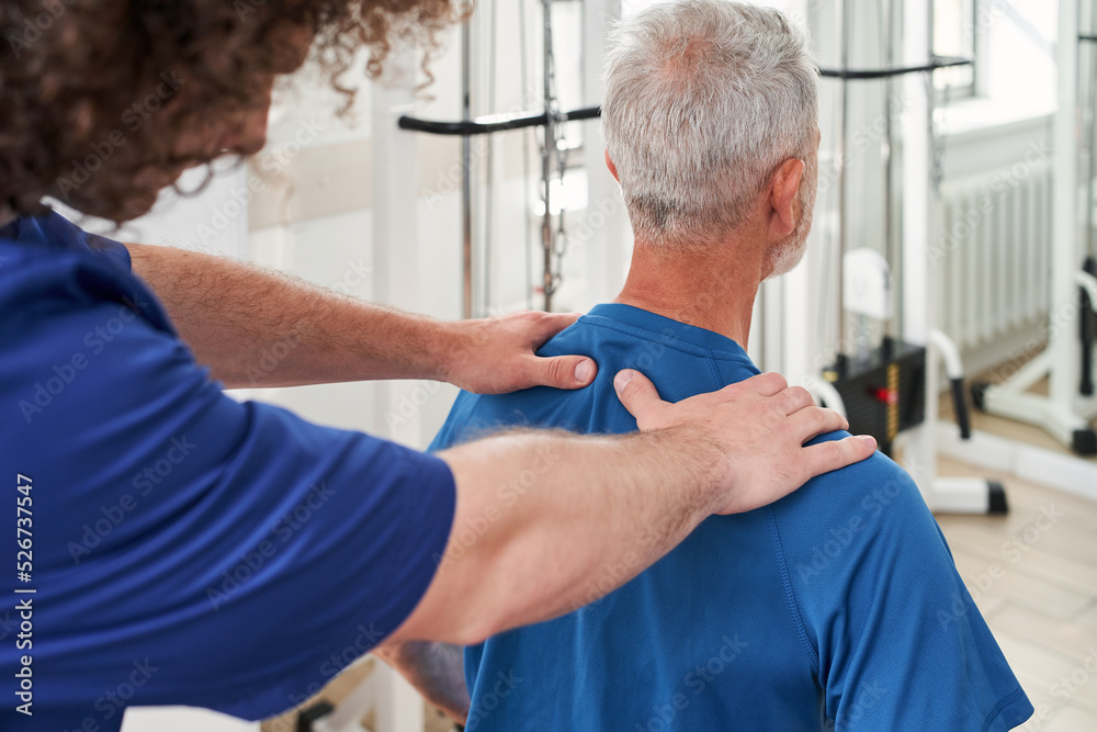 Obraz premium Male physiotherapist working on elderly man's tension his shoulders