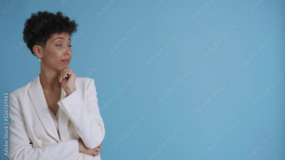Pretty hispanic curly haired woman wearing white jacket looking at the copyspace in the blue studio