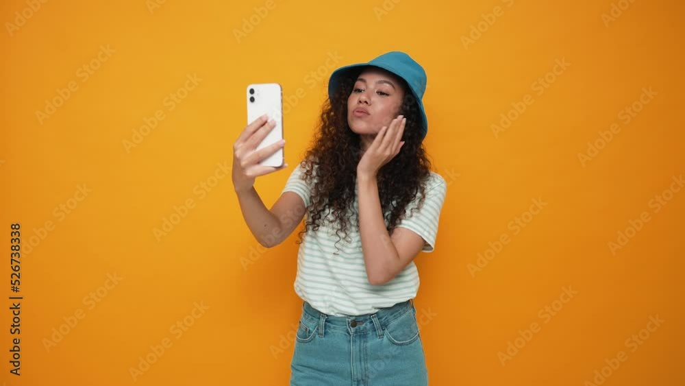 Handsome brunette curly haired woman wearing panama hat making selfie on mobile in the yellow studio Handsome brunette curly haired woman wearing panama hat making selfie on mobile in the yellow studio