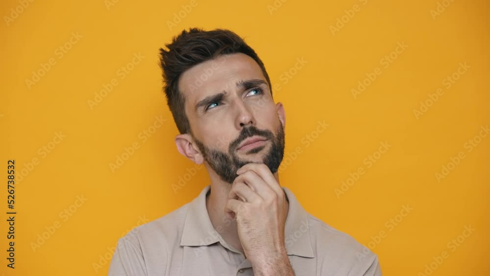Confident brunet man wearing t-shirt thinking about something while standing in the yellow studio Confident brunet man wearing t-shirt thinking about something while standing in the yellow studio