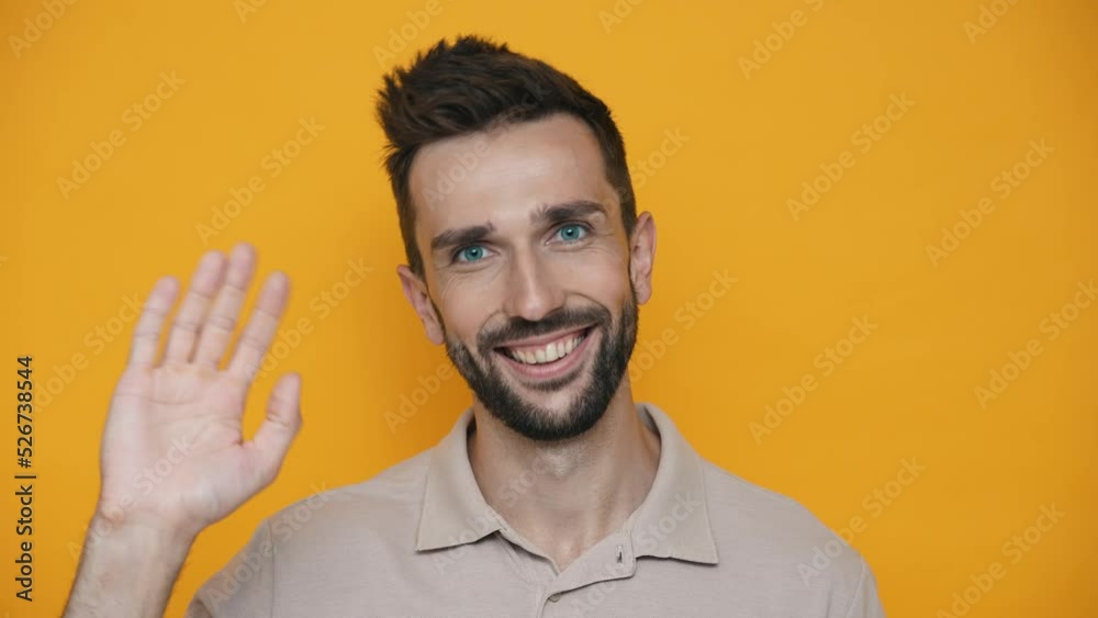 Pretty brunet man wearing t-shirt waving hand at the camera while standing in the yellow studio Pretty brunet man wearing t-shirt waving hand at the camera while standing in the yellow studio