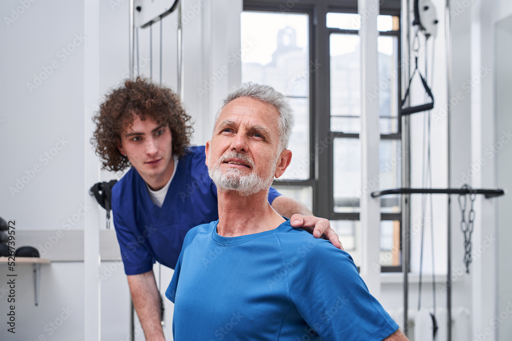 Qualified young physiotherapist assessing muscle strength of senior patient while training Qualified young physiotherapist assessing muscle strength of senior patient while training
