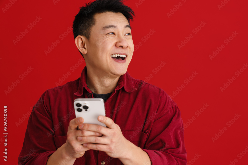 Asian young man wearing shirt laughing while using mobile phone Asian young man wearing shirt laughing while using mobile phone
