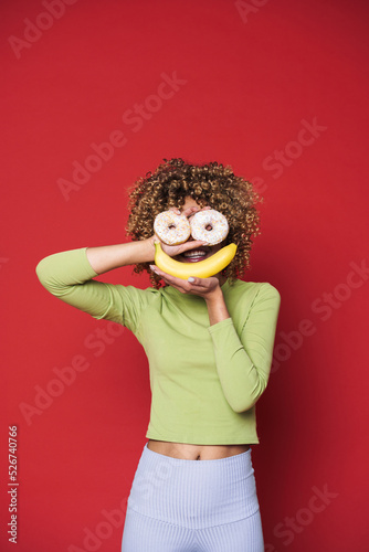 Young black woman with afro curls having fun holding donuts and banana