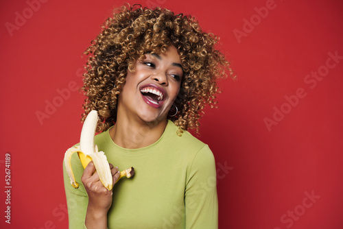 Young black woman with afro hairstyle laughing while eating banana © Drobot Dean