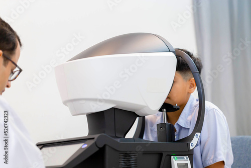 Boy doing eye test checking examination with autorefractor in optical shop, Optometrist doing sight testing for child patient, Eye doctor examinating kid patient photo