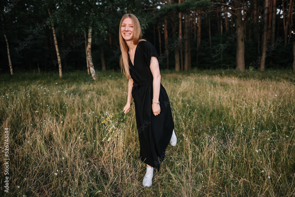 beautiful young girl in black dress and with long hair is resting in nature