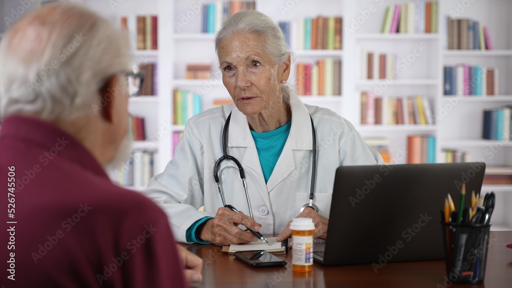 Mature senior female doctor talking to male patient in modern clinic with library background. Mature senior female doctor talking to male patient in modern clinic with library background.