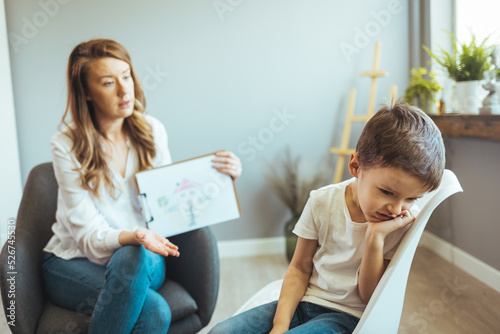 Young Boy Talking With Counselor At Home. Female psychologist working with little boy in office. Young female school psychologist having serious conversation with smart little boy
