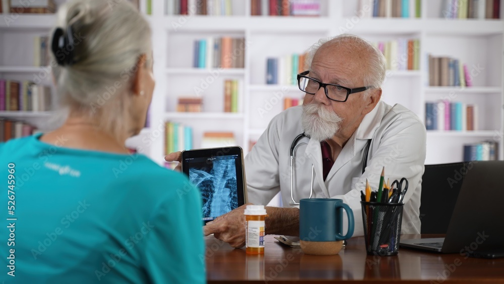 Mature senior male doctor discussing treatment with prescription drug to female patient in modern clinic with books background. Mature senior male doctor discussing treatment with prescription drug to female patient in modern clinic with books background.