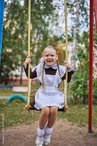 little girl schoolgirl happy rides on a swing in the yard on the playground.