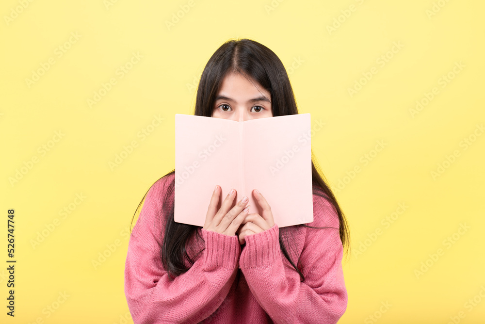 Portrait of a cheerful girl covering her face with a pink textbook. Has a cheerful mood when reading her favorite stories, likes novels, spends her free time on hobbies. isolated from the pink backgro Portrait of a cheerful girl covering her face with a pink textbook. Has a cheerful mood when reading her favorite stories, likes novels, spends her free time on hobbies. isolated from the pink backgro