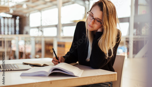 Focused woman studying at desk in university library © Timm Creative