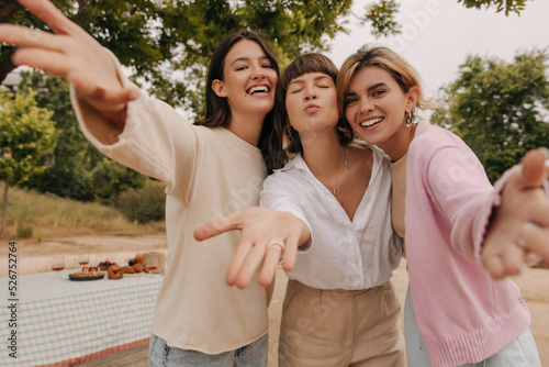 Positive young caucasian women stretch their hands to camera relaxing outdoors. Girlfriends smile, wear casual clothes. Spring season concept