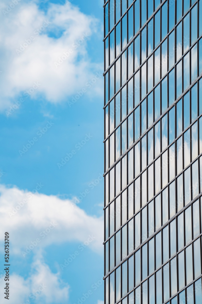 glazed facade of a high-rise building against a blue sky with clouds glazed facade of a high-rise building against a blue sky with clouds