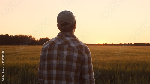 Farmer in front of a sunset agricultural landscape. Man in a countryside field. Country life, food production, farming and country lifestyle concept. © Acronym