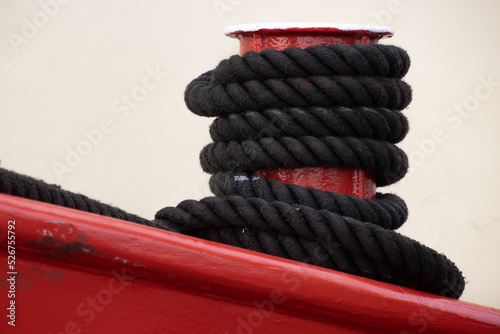 Black rope tied to a red metal mooring bollard photo