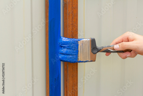 Painting rust with blue paint for metal.The hand paints the crossbars of the fence. photo