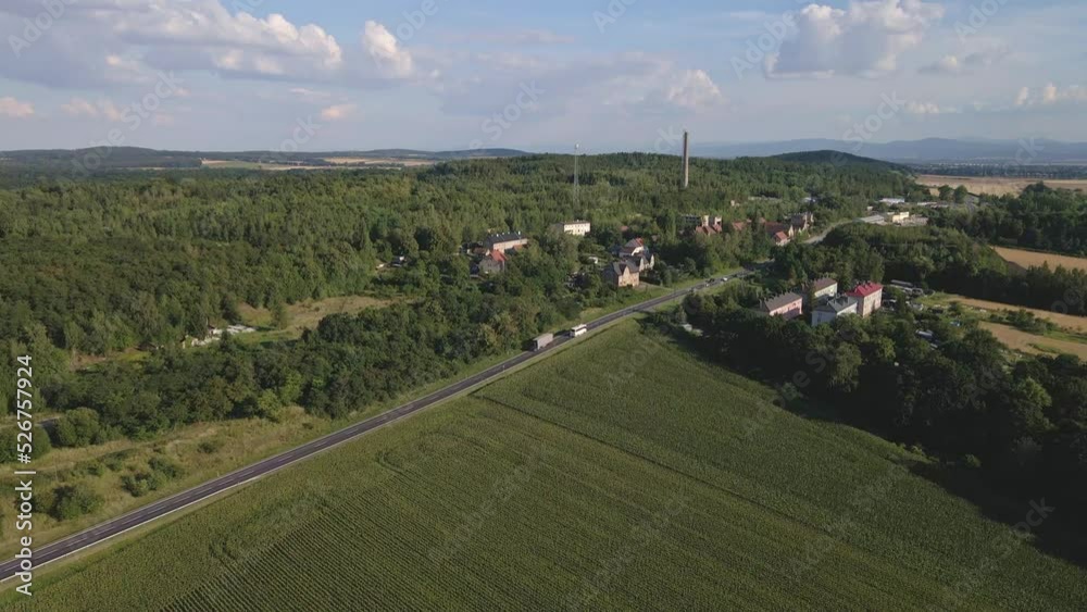 Aerial view of rural road with car moving along it. Car traffic on countryside highway near small village and mountain background Aerial view of rural road with car moving along it. Car traffic on countryside highway near small village and mountain background