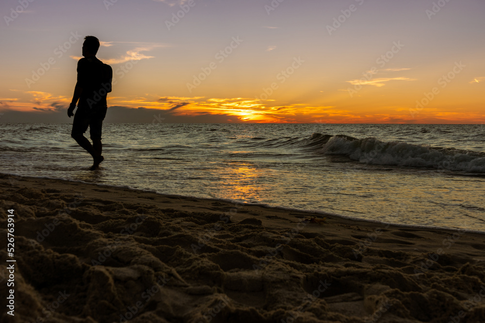A man walking along the seashore during the sunset