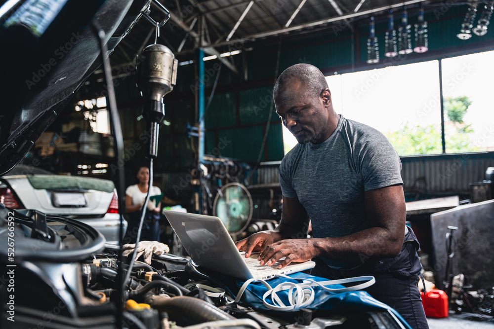 Mechanic checking the engine and using the computer to record the data. Mechanic checking the engine and using the computer to record the data.
