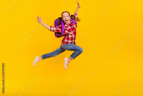 Photo of sweet impressed schoolkid dressed plaid shirt jumping high running fast empty space isolated yellow color background © deagreez