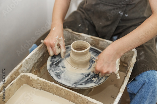 Potter girl works on potter's wheel, making ceramic pot out of clay in pottery workshop. Art concept