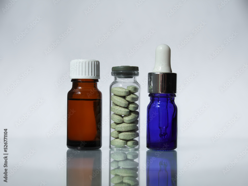 There are a glass jar with green pharmaceutical pills, blue pipette with medical drops and brown medical bottle with oil on the mirror background There are a glass jar with green pharmaceutical pills, blue pipette with medical drops and brown medical bottle with oil on the mirror background