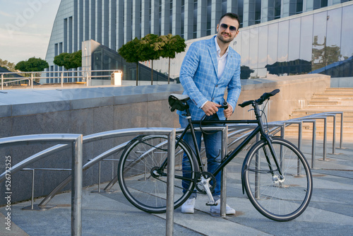 Fototapeta Naklejka Na Ścianę i Meble -  Shot of stylish businessman with bicycle outdoors in daytime against huge city building.
