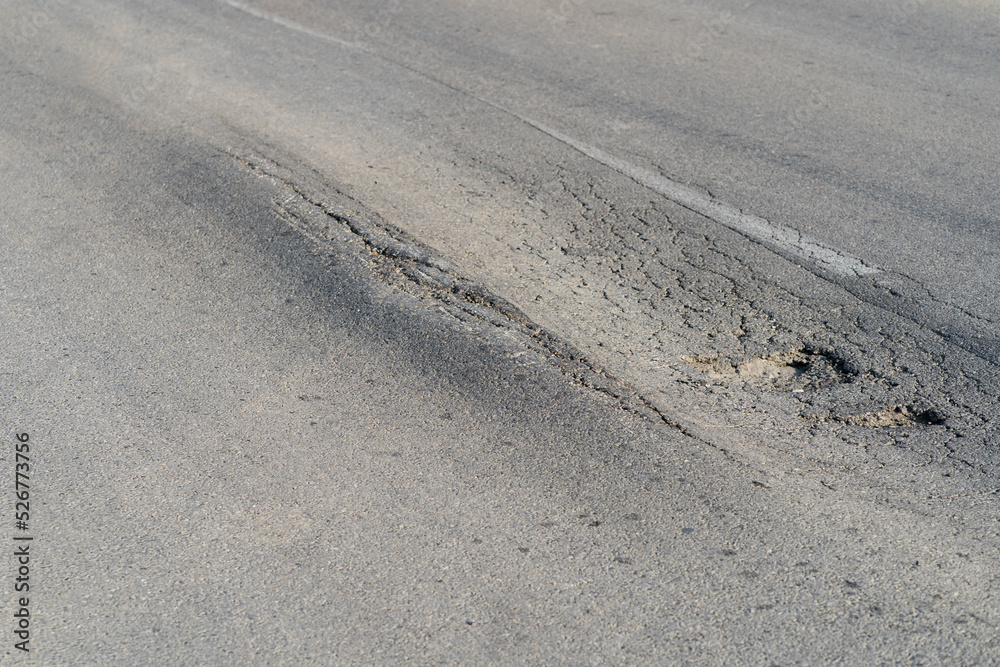 Broken road with holes and cracks built in countryside on hot sunny day. Deformed and expanded asphalt surface with potholes caused by heavy overloaded trucks driving on highway at rural site closeup