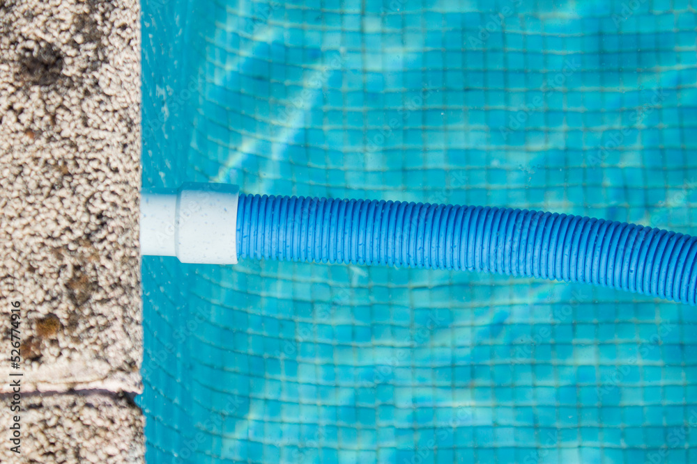 A connected blue pool cleaner hose floats in the pool water next to the stone curb. Pool cleaning and maintenance.