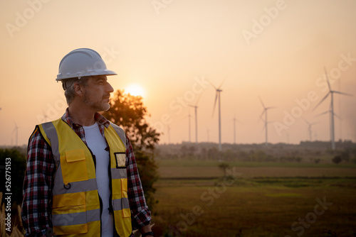 Portrait of engineer wearing yellow vest and white helmet on site at wind turbines field or farm, Sustainable energy concept